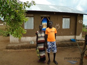 Figure  SEQ Figure \* ARABIC 2 Joyce and her son pause in front of their shelter constructed by PWJ